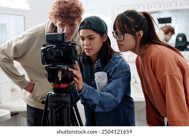 Group of young diverse individuals working together while setting up professional camera in modern studio environment. Enthusiastic team reviewing footage on camera screen - Powered by Shutterstock