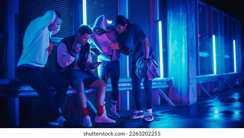 Group of Young Diverse Men Watching a Sports Game on Smartphone Device, Cheering for Their Favorite Team. Celebrating Goal, Betting or Lottery Win. Standing Outside in Urban Location with Neon Lights - Powered by Shutterstock