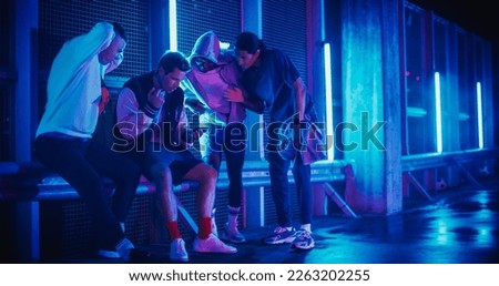 Group of Young Diverse Men Watching a Sports Game on Smartphone Device, Cheering for Their Favorite Team. Celebrating Goal, Betting or Lottery Win. Standing Outside in Urban Location with Neon Lights