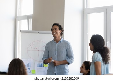 Group Of Young Diverse Staff Member Take Part In Corporate Training Led By Hispanic Business Trainer, Makes Presentation On Flip Chart. Seminar Event, Professional Workshop Activity, Coaching Concept