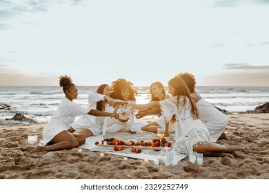 Group of young diverse women toasting with champagne, having bachelorette party celebration on the beach, enjoying picnic at sunset, free space - Powered by Shutterstock