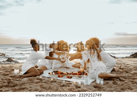 Group of young diverse women toasting with champagne, having bachelorette party celebration on the beach, enjoying picnic at sunset, free space