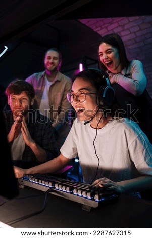 Group of young emotional people watching their friend playing online video game and assisting her in modern cybersport club
