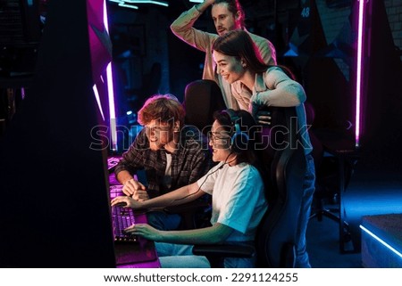 Group of young emotional people watching their friend playing online video game and assisting her in modern cybersport club