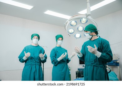 Group Of Young And Experienced Male And Female Surgeon With Nurse And Doctor Wearing Scrub, Mask And Headscarf Operating Young Woman In Operation Theatre In Modern Hospital