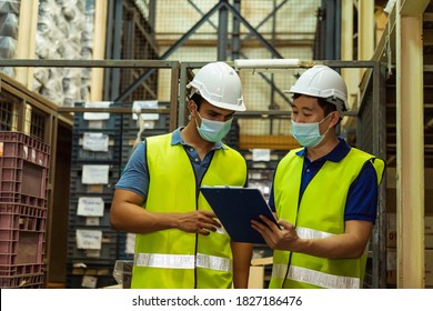 Group Of Young Factory Warehouse Workers Wearing A Protective Face Mask While Working In Logistic Industry Indoor. Asian And Indian Ethnic Men Checking Item Order During Coronavirus Covid 19 Pandemic