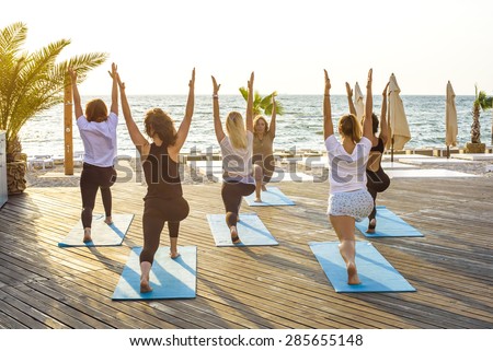 group of young females practicing yoga on the seaside during the sunrise
