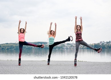 A group of young fit slim women in kangoo jumps, training in front of city lake in summer. Three sportswomen, wearing colorful sports outfit, doing exercises outside. Healthy lifestyle concept.