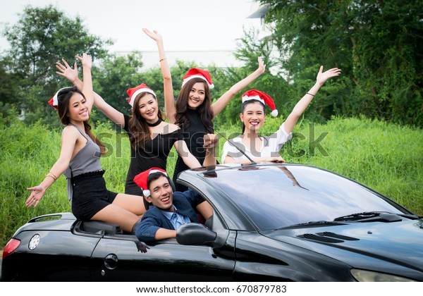 Group of young friends In back of open top car,Santa\
christmas woman smiling portrait, A lovely friends is going on\
vacation in a convertible sport car,They drive on a country road on\
a sunny day,
