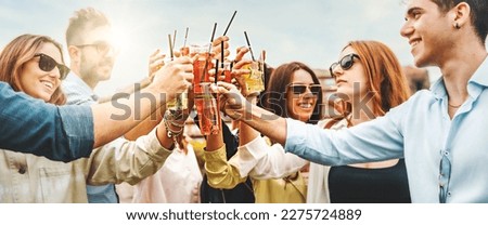Group of young friends in casual outfits toasting with various colorful cocktails outdoors. Bright sunny day and white background