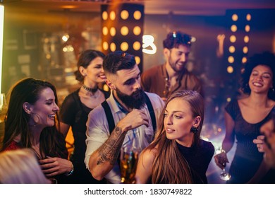 Group of young friends dancing together in the nightclub surrounded by confetti
