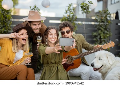 Group Of Young Friends With Drinks Having Fun Together, Making Selfie Or Having A Video Call On Phone At Backyard Outdoors