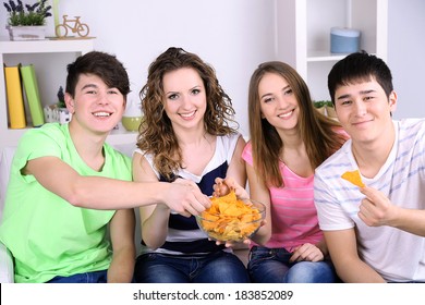 Group Of Young Friends Eating Chips In Living-room On Sofa