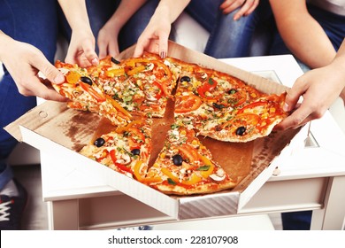 Group Of Young Friends Eating Pizza In Living-room On Sofa