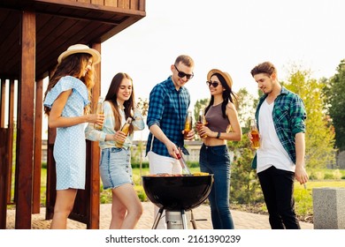 A group of young friends hang out by the fireplace, excited by the huge fire in the backyard. Barbecue in a friendly company near a country house, a group of friends on a picnic fry shish kebabs