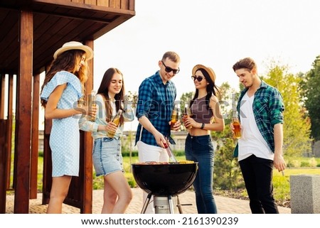 A group of young friends hang out by the fireplace, excited by the huge fire in the backyard. Barbecue in a friendly company near a country house, a group of friends on a picnic fry shish kebabs