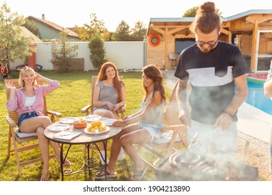 Group Of Young Friends Having A Backyard Barbecue Party, Grilling Meat And Having Fun While Spending Sunny Summer Day Outdoor By The Swimming Pool