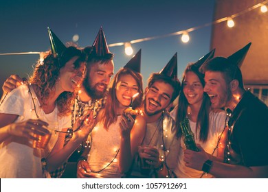 Group Of Young Friends Having A Birthday Party At A Building Rooftop, Singing A Song And Blowing A Candle. Focus On The Candle And People On Sides