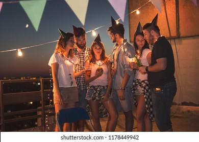 Group of young friends having a birthday party at a building rooftop, all bored and serious. Focus on the birthday girl