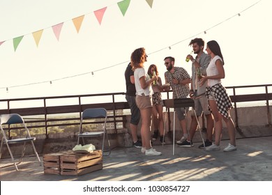 Group of young friends having fun at rooftop party, making barbecue and enjoying hot summer days. Focus on the guy in the middle - Powered by Shutterstock