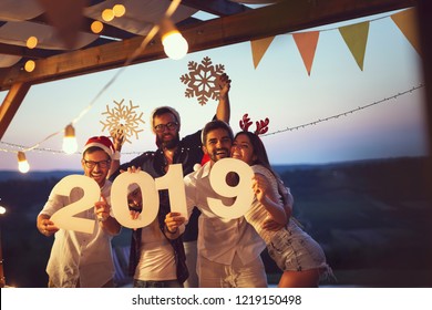 Group of young friends having fun at a New Year's Eve outdoor pool party, dancing and holding cardboard snowflakes and numbers 2019. Focus on the couple on the right - Powered by Shutterstock