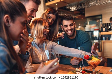 Group of young friends having fun in restaurant, they are looking at smartphone and making selfie. - Shutterstock ID 1342981190