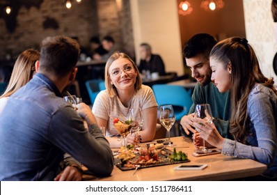 Group Of Young Friends Having Fun In Restaurant, Talking And Laughing While Dining At Table.