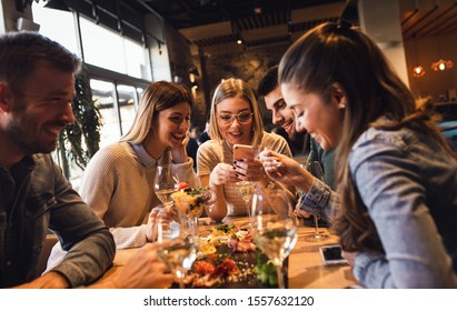 Group of young friends having fun in restaurant, talking and laughing while dining at table.