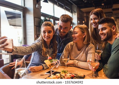 Group of young friends having fun in restaurant talking, laughing while dining at table and making selfie. - Shutterstock ID 1557634592