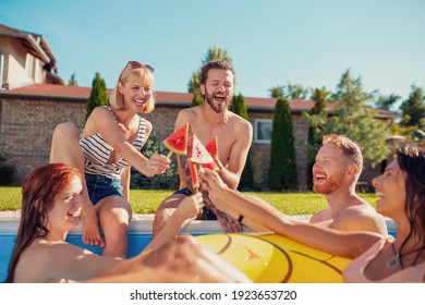 Group of young friends having fun at summertime swimming pool party, sitting by the pool and eating watermelon popsicles, spending sunny summer day outdoors - Powered by Shutterstock