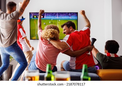 Group of young friends having fun watching football match on TV, drinking beer and cheering; football fans watching game at home celebrating after their team scoring a goal