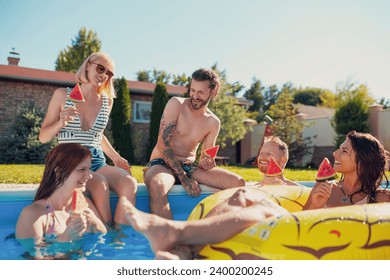 Group of young friends having fun at summertime swimming pool party, sitting by the pool and eating watermelon popsicles, spending sunny summer day outdoors - Powered by Shutterstock