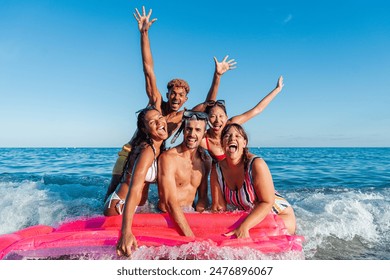Group of young friends having fun at the beach, floating on an inflatable mattress by the sea shore. Multiracial people smiling and looking at the camera on the coast, enjoying the summer vacations - Powered by Shutterstock