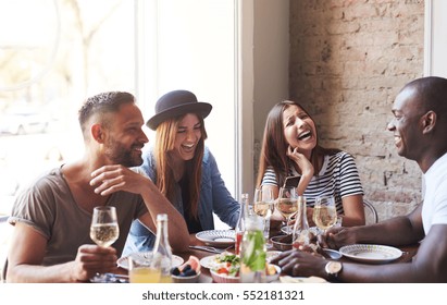 Group of young friends having fun and laughing while dining at table in restaurant.