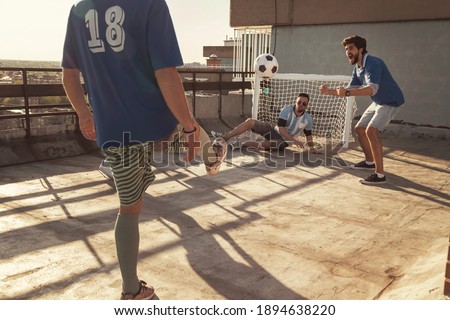 Group of young friends having fun playing football on a building rooftop, winning team celebrating after  scoring a goal