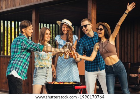 Group of young friends having fun at a party outdoors, drinking cold drinks, making barbecue and grilled vegetables, enjoying hot summer days,