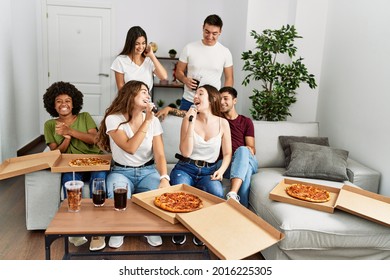 Group of young friends having party eating italian pizza and singing song at home. - Powered by Shutterstock