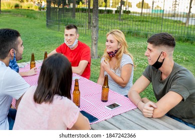 Group Of Young Friends Organize A Picnic At The Park With Beers, New Ways To Socialize In Time Of Coronavirus Epidemic, People Wearing Protective Masks, Breaking The Rules Of Social Distancing