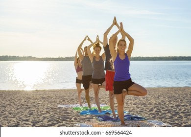 Group Of Young Friends Practicing Yoga On A Beach