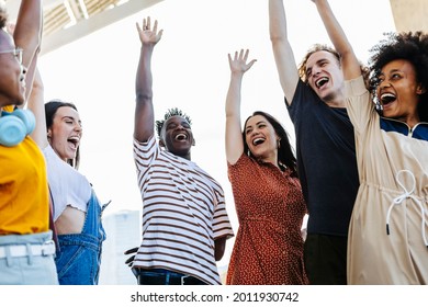 Group of young friends raising their hands in unity - Happy multiracial people having fun together outdoors - Low angle view - Unity, integration and community concept - Focus on hispanic woman - Shutterstock ID 2011930742