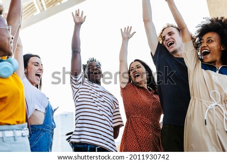 Group of young friends raising their hands in unity - Happy multiracial people having fun together outdoors - Low angle view - Unity, integration and community concept - Focus on hispanic woman