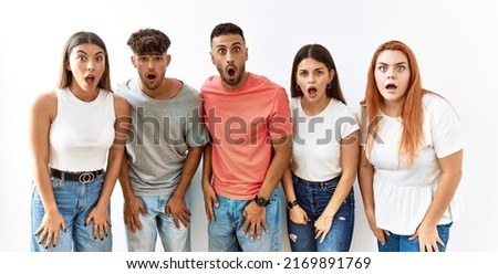 Group of young friends standing together over isolated background afraid and shocked with surprise and amazed expression, fear and excited face. 