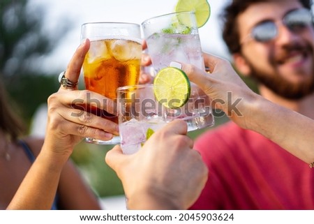 Group of young friends toasting outdoors. Focus on glasses, blurred faces. 