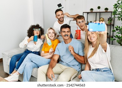 Group of young friends using funny costume accessories making selfie by the smartphone at home.