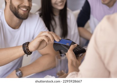 Group of young friends visited public place pay for services, food or goods using credit card and payment terminal machine, close up crop view. Cashless checkout, spend money use modern NFC technology