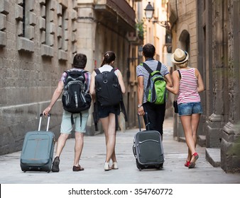 Group Of Young Friends Walking Through The City With Travel Bags. Back View
