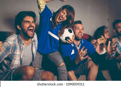 Group of young friends watching a football match on a building rooftop, celebrating after their team has scored a goal. Focus on the man in the middle.
