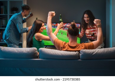 Group Of Young Friends Watching A Football Match On TV Together And Cheering For Their Team