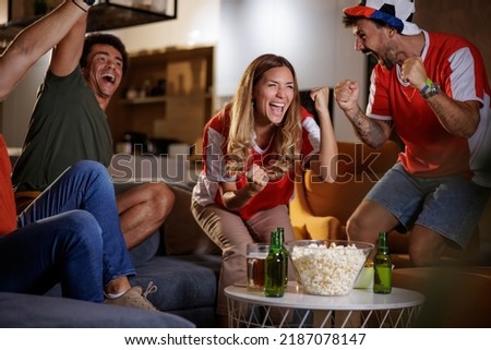 Group of young friends watching football match, celebrating after their team has scored a goal