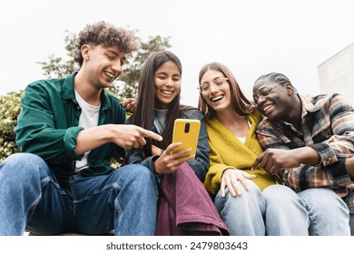 Group of young Gen Z friends sitting together using cell phone app to share funny social media content - Powered by Shutterstock